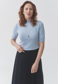Light blue short-sleeve pullover top with a ribbed neckline, paired with a dark, knee-length skirt featuring side buttons.