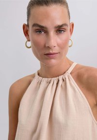 Top halter de color melocotón con escote fruncido, tejido texturizado y tirantes finos. Presenta un diseño simple y elegante sin adornos adicionales.