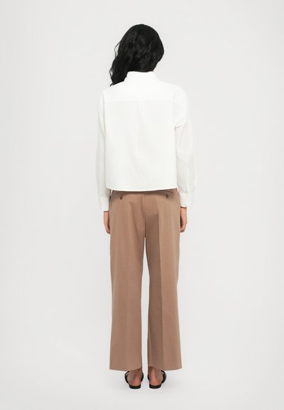 Chemise blanche courte avec col haut, associée à un pantalon beige à jambes larges. La tenue présente un design épuré et des textures douces.