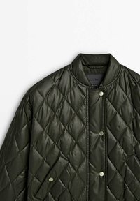 Pikowana oliwkowozielona kurtka w diamentowy wzór, okrągły kołnierz, zapięcia na zatrzaski oraz boczne kieszenie. Wykonana z błyszczącego, gładkiego materiału.