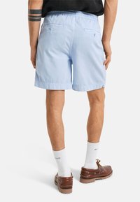Lyseblå shorts med elastisk midje, sideslag og to baklommer. Kombinert med hvite sokker og brune sko.