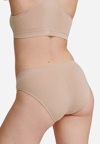 Beige sömlös bralette med tunna band och matchande höga trosor. Mjukt, stretchy material med minimal detalj för komfort.