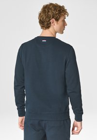 Felpa blu navy con colletto a coste, maniche lunghe e una piccola etichetta colorata sul retro. Realizzata in un tessuto morbido con una texture liscia.