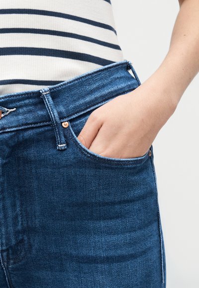 Χέρι με δάχτυλα μέσα στην εμπρόσθια τσέπη μπλε τζιν, φορεμένο με λευκό και ναυτικό ριγέ τοπ.