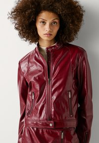 Rode glanzende faux leren jas met ritszakken, een staande kraag en een asymmetrische rits aan de voorkant, met een getailleerd ontwerp.