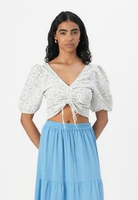 Vit blommig cropped topp med puffärmar och dragsnörning fram, parat med en ljusblå, flera lager lång kjol gjord av lätt tyg.
