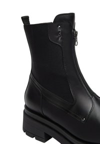 Stivale alla caviglia in pelle nera con zip laterale, pannello elastico, linguetta sul retro e piccolo logo metallico vicino alla parte superiore.