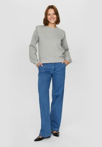 Szürke crew-neck pulóver, texturált felülettel, kék bőszárú farmernadrággal és fekete, hegyes orrú balerina cipővel párosítva. Hétköznapi öltözet semleges színekben.