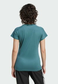 Teal kortemouwen t-shirt met een zachte textuur en een aangesloten ontwerp. Heeft een ronde halslijn en gladde naden, in combinatie met zwarte trainingsbroek.