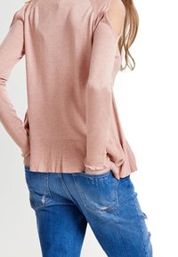 Helles pinkes Langarmoberteil mit Cutouts an den Schultern, geripptem Saum und strukturierten Ärmeln, kombiniert mit zerrissenen blauen Jeans.