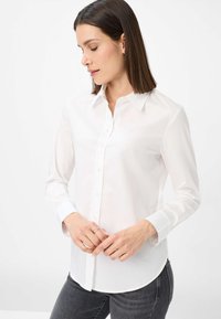 Weißes Hemd mit langen Ärmeln, klassischer Kragen und geradem Saum. Der Stoff wirkt glatt, leicht und leicht durchsichtig.