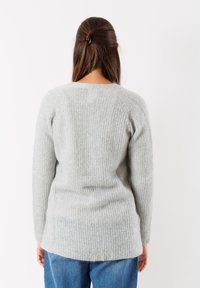 Maglione a maglia grigio chiaro con una texture a costine. Presenta maniche lunghe, un collo rotondo e un orlo posteriore leggermente più lungo.
