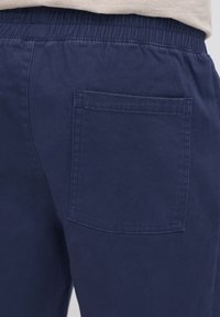 Tamsiai mėlynos kelnės su elastine juosmens juosta, vienu atgaliniu kišene. Pagamintos iš lygaus audinio su švariu, paprastu dizainu.