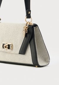 Crna i bež strukturirana torba od teksturiranog materijala, s hardverom u zlatnoj boji i odvojivim remenom. Ukrašena jedinstvenim kopčom.