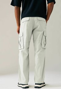 Pantalones cargo de color gris claro, hechos de una tela suave, con múltiples bolsillos laterales y un corte relajado, combinados con zapatillas negras y blancas.