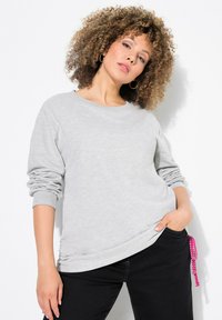 Felpa grigia con maniche lunghe, scollatura a girocollo e dettaglio arricciato all'orlo. Abbinata a pantaloni neri con cordino rosa.