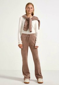 Kremfarvet langærmet skjorte, lysebrune bløde sweatpants med snøre samt matchende tørklæde om halsen. Hvide sneakers.