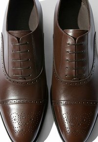 Scarpe eleganti in pelle marrone con una finitura lucida, caratterizzate da perforazioni dettagliate e un classico design con lacci. Punta arrotondata e cuciture eleganti.