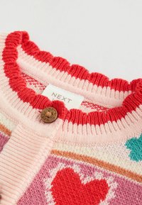 Strickjacke mit einem gewellten roten Kragen, verziert mit Herzen und geometrischen Mustern in Pink, Rot und Teal, verschlossen mit einem runden braunen Knopf.