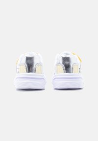 Ζευγάρι λευκά αθλητικά παπούτσια με μεταλλικές ασημένιες λεπτομέρειες στη φτέρνα και μπεζ λεπτομέρειες σε λευκό φόντο, ορατά από πίσω.