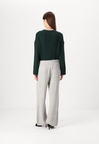 Maglione a maniche lunghe verde scuro a trecce abbinato a pantaloni a gamba larga grigio chiaro a coste, entrambi con motivi testurizzati e una vestibilità rilassata.