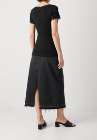 Top negro con bordado de encaje en las mangas, combinado con una larga falda de mezclilla negra con una abertura en la parte trasera y dobladillo deshilachado. Llevado con mules negros de tacón.