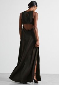 Schwarzes Maxikleid mit ausgeschnittenem Rücken, goldfarbigen Akzentverzierungen, seitlichen Schlitzen, ärmellosem Design, glatter Textur und knielangem Unterlayer.