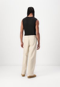 Svart ermeles topp med rund hals, beige vide bukser med elastisk midje, og lysebrune slip-on sko, sett bakfra.