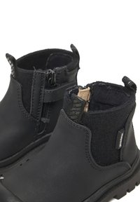 Stivaletti neri alla caviglia con esterno in pelle liscia e fodera in feltro. Presentano un pannello laterale testurizzato e due cerniere per una facile calzata.