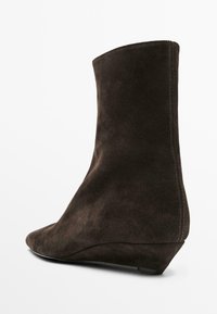 Bottine en suede marron avec un talon compensé, présentant une texture lisse, une pointe effilée et un design épuré sans quincaillerie visible.