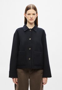 Casaco de mistura de lã preta com gola com colarinho, fecho frontal com botões e dois bolsos. Apresenta mangas largas e um design cropped.