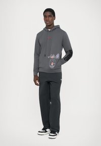 Gray hoodie made of cotton blend, featuring a graphic design on the front and a textured black print on the left sleeve, paired with black pants.