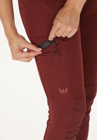 Bordeauxfarbene Performance-Hosen mit einer Reißverschlusstasche und Mesh-Futter. Sie zeichnen sich durch ein angelegtes Design und ein Logo am Oberschenkel aus. Glattes, dehnbares Material.