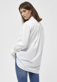 Camicia bianca a maniche lunghe con vestibilità rilassata e orlo arrotondato, realizzata in un morbido tessuto misto cotone. Caratterizzata da polsini con bottone e un'unica tasca sul petto.