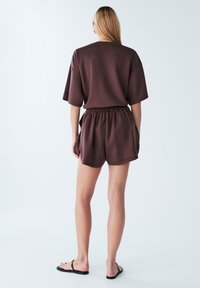 Pantaloni corti in jersey marrone con vita elastica e una maglietta oversize a maniche corte, caratterizzata da una texture liscia e una vestibilità rilassata.