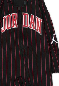 Tutina nera con righe rosse, presenta "JORDAN" in lettere bianche, include una chiusura con zip e un logo Jumpman bianco sulla manica.