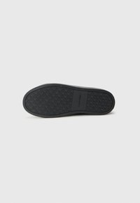 Talpa de pantof din cauciuc negru cu un model texturat de aderență și logo-ul „Calvin Klein” embossat. Formă curbată cu o finisare netedă.