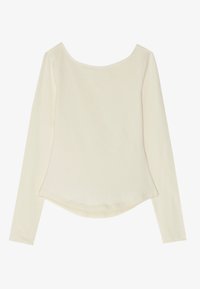 Long-sleeve top in soft, cream-colored fabric with a rounded neckline and a curved hem, featuring a smooth, slightly stretchy texture.