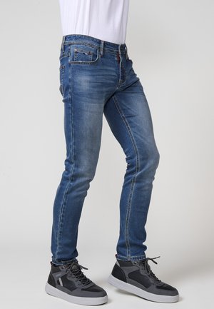 Jeans slim fit de mezclilla azul con un lavado desvaído, diseño de cinco bolsillos y costuras en contraste, combinados con zapatillas altas grises.