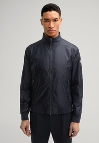 Marineblauer gefütterter Bomberjacke mit strukturiertem Muster, hohem Kragen und Fronttaschen. Aus leichtem, glattem Material gefertigt.
