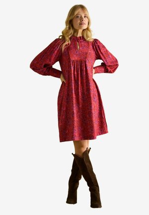 Red floral-patterned dress with a high neckline, puffed sleeves, and a keyhole detail. Paired with brown knee-high boots.