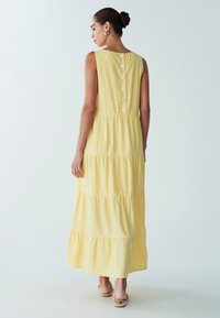 Geltona, sluoksniuota maxi suknelė iš minkštos medžiagos. Turi apvalų kaklo iškirpimą, sagą užsegimą nugaroje ir be rankovių.