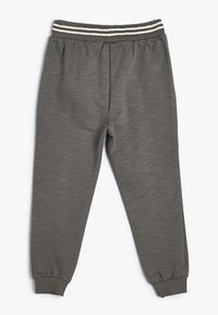 Grijze joggingsbroek met een gestructureerde afwerking, elastische tailleband met twee witte strepen en aansluitende boorden bij de enkels.