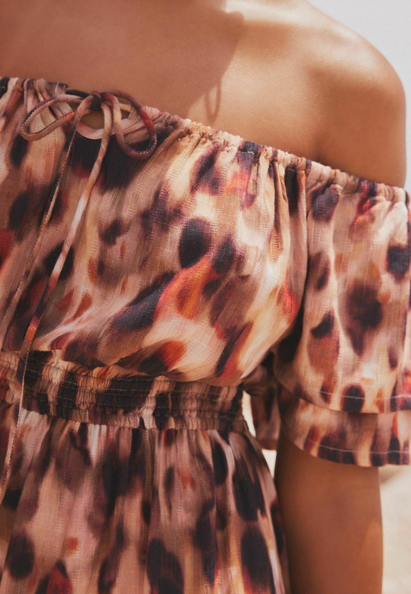 Gros plan d’une personne portant une robe à épaules dénudées avec un col froncé et un motif abstrait marron, noir et orange.