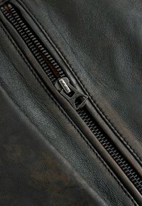 Gros plan d'une surface en cuir noir avec une fermeture éclair métallique noire partiellement ouverte, dents et tirette visibles.