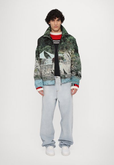 Collared jacket with a nature graphic, predominantly green and blue, paired with light blue jeans and white sneakers. Features bold red-accented cuffs.