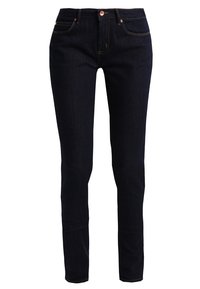 Los jeans de mezclilla oscura presentan un corte ajustado, con costuras destacadas y un diseño clásico de cinco bolsillos. La cinturilla tiene un cierre de botón.
