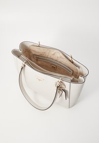Lys beige håndveske med en strukturert form, utstyrt med gullfarget detaljer, glidelås-lukking og et interiør foret med et logomønster.