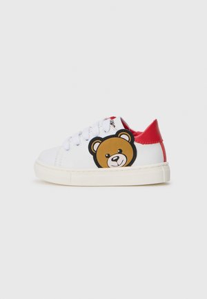 Zapatilla blanca con tacón rojo, que presenta un gráfico de un oso marrón en el lado, cierre de cordones y suela de goma texturizada.