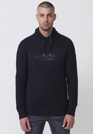 Sudadera azul marino con tejido texturizado, capucha con cordones y un logo en el pecho. Presenta puños y dobladillo acanalados para un ajuste ceñido.